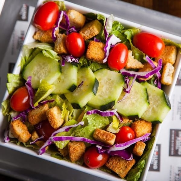 A fresh side salad with lettuce, cucumbers, tomatoes, red cabbage, and croutons.