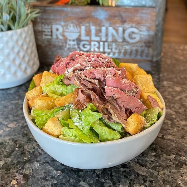 Caesar salad with shaved pit beef, croutons, and parmesan cheese in a white bowl.
