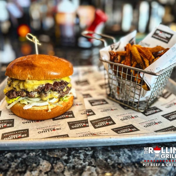 A double cheeseburger with onions and cheese, served with a side of fries in a metal basket.