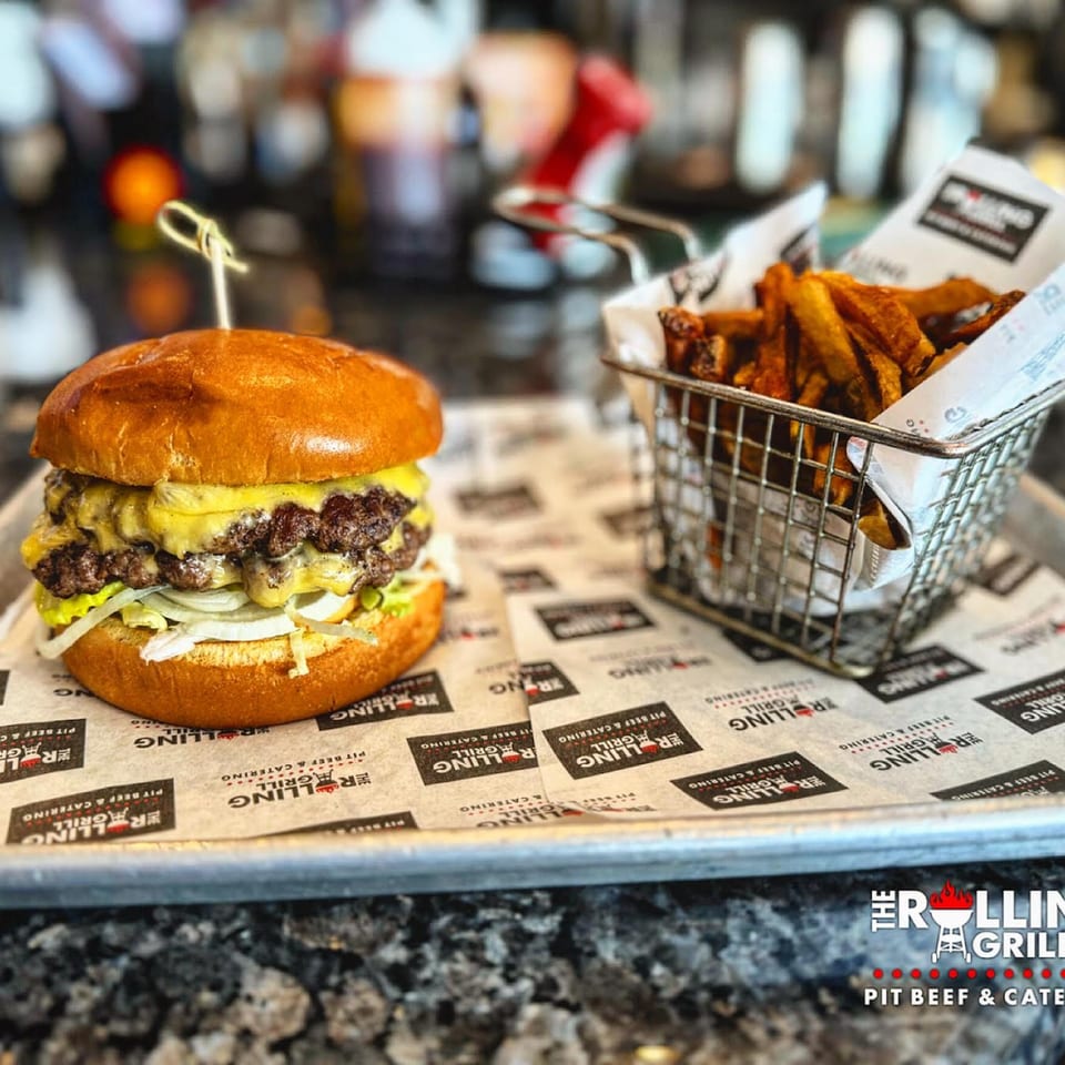 A double cheeseburger with onions and cheese, served with a side of fries in a metal basket.