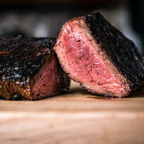 Two thick slices of perfectly cooked pit beef, showing a dark crust and juicy pink interior.