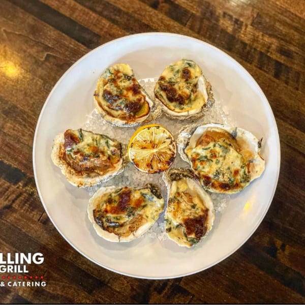 Six baked oysters with melted cheese and herbs, garnished with a grilled lemon slice on a white plate.