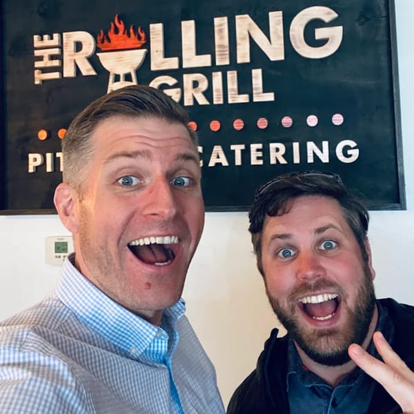 Two excited men with wide open mouths in front of The Rolling Grill Pit Beef sign.